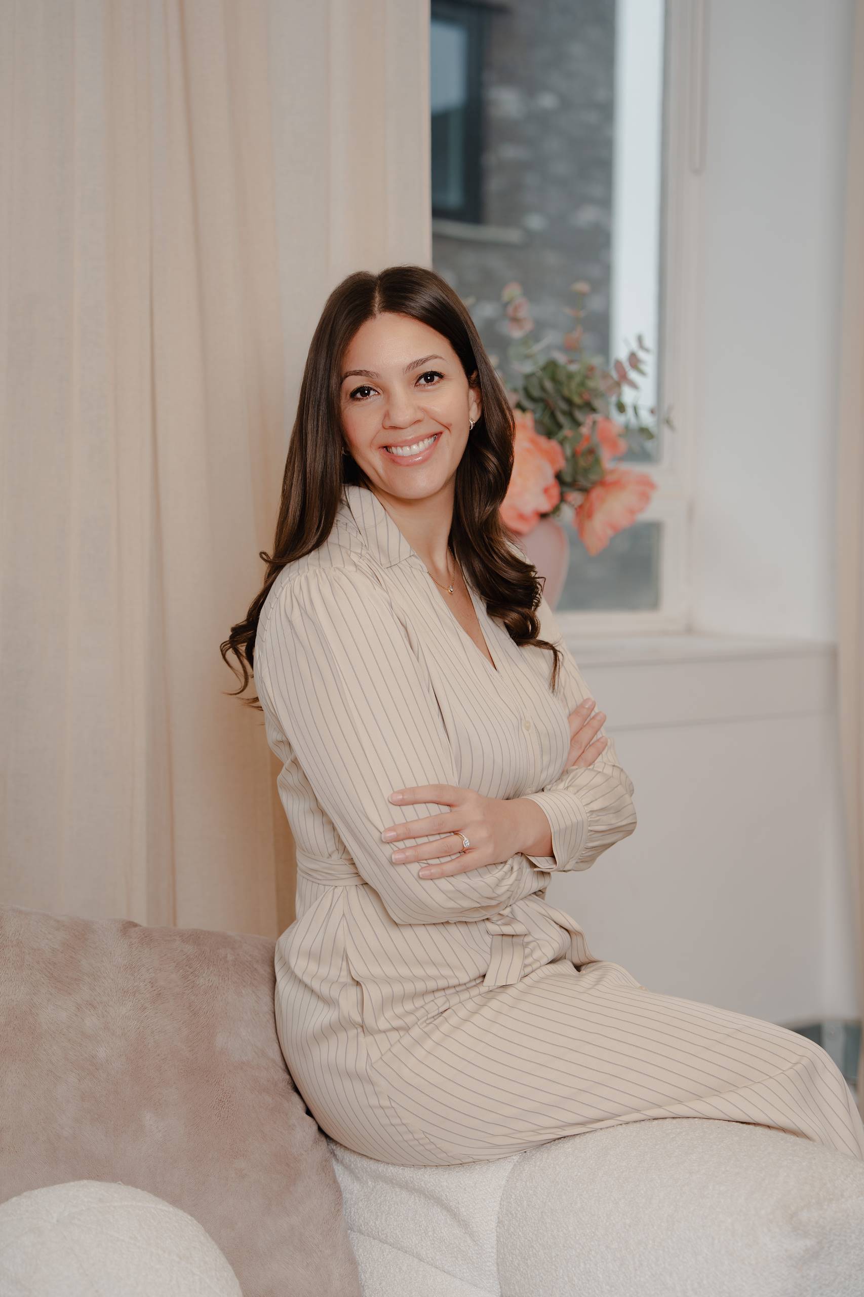 Dominique Hendrickson-Gerrick seated with folded arms, wearing a cream dress.