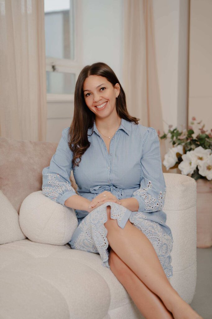 Dominique Hendrickson-Gerrick seated on a sofa, wearing a blue and white dress.